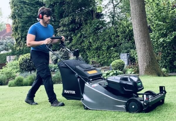 Professional gardener mowing a large residential lawn with a Hayter Harrier 56 Pro 60V battery mower, creating deep green stripes.