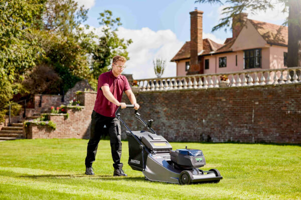 Professional gardener mowing a large residential lawn with a Hayter Harrier 56 Pro 60V battery mower, creating deep green stripes.