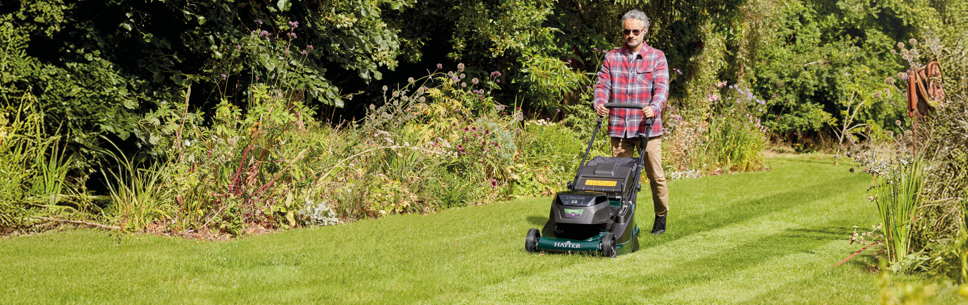 Man mowing a lawn with the Hayter Harrier 56 60V cordless lawnmower. Promotional offer includes 2x free 7.5Ah batteries on purchases made between 1 March and 31 July 2025.