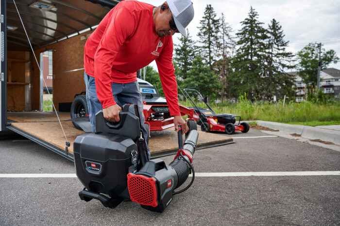 Operator connecting Toro Revolution Blower Cannon to Backpack unit outside trailer