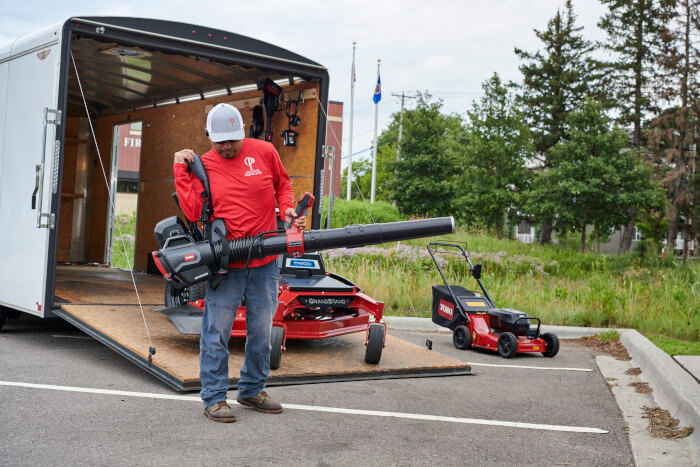 Professional user preparing Toro Revolution Backpack & Blower for use beside landscape trailer