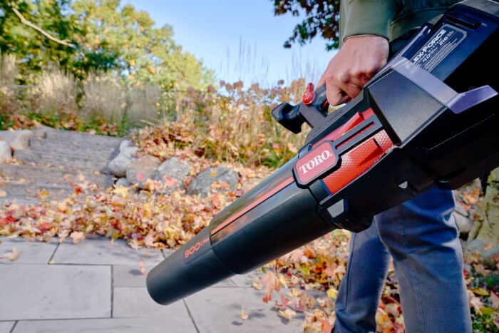 Toro Leaf Blower Plus in use, blowing a pile of autumn leaves mid-air