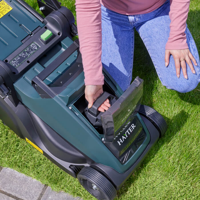 Person inserting a 60V Flex-Force battery into a Hayter cordless lawnmower on grass